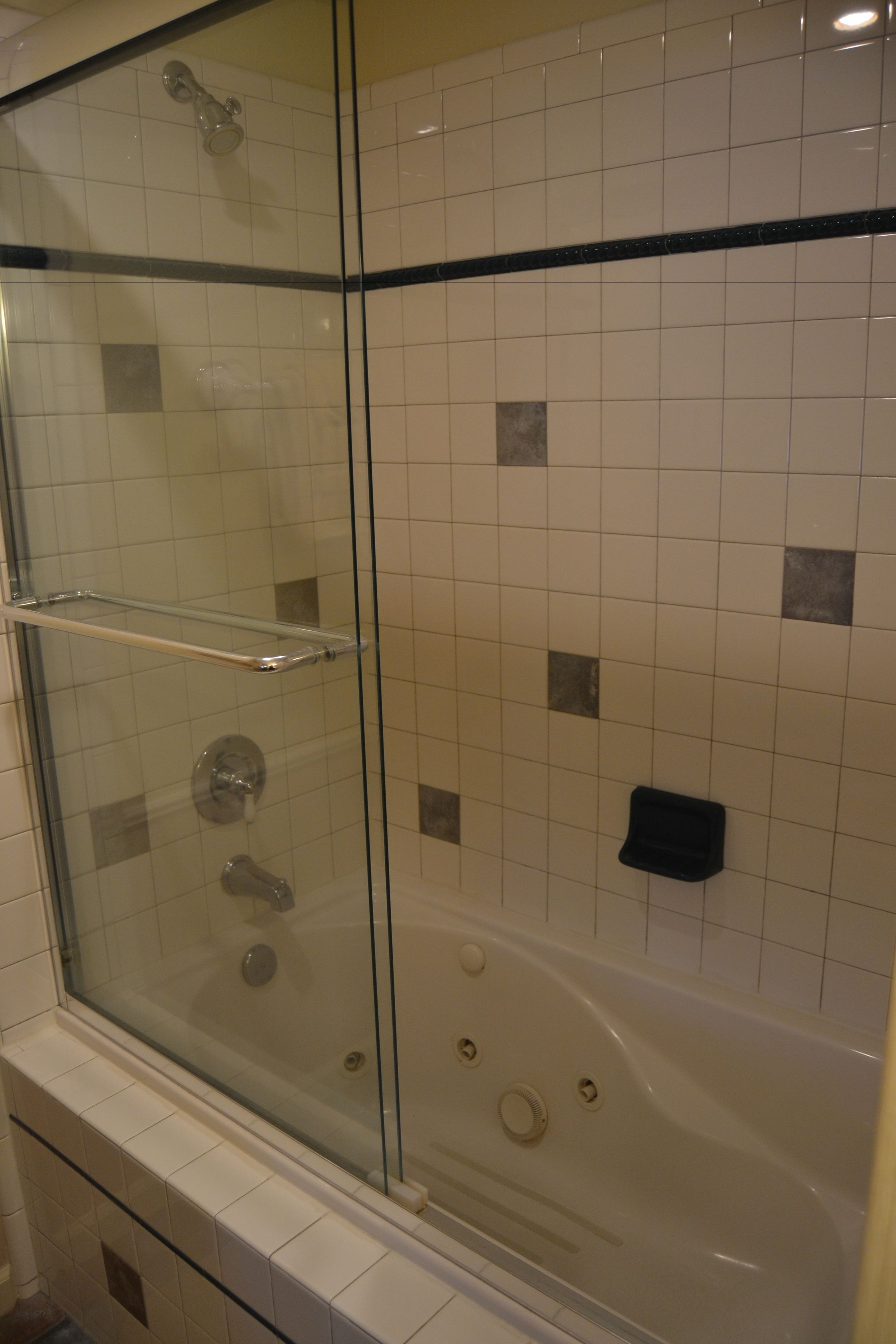 Ducha con mampara de vidrio, bañera y pared con revestimiento de azulejos y borde negro.