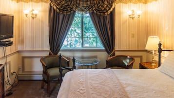Habitación de hotel con una cama grande, dos sillas, una mesita, un televisor y una ventana con cortinas.