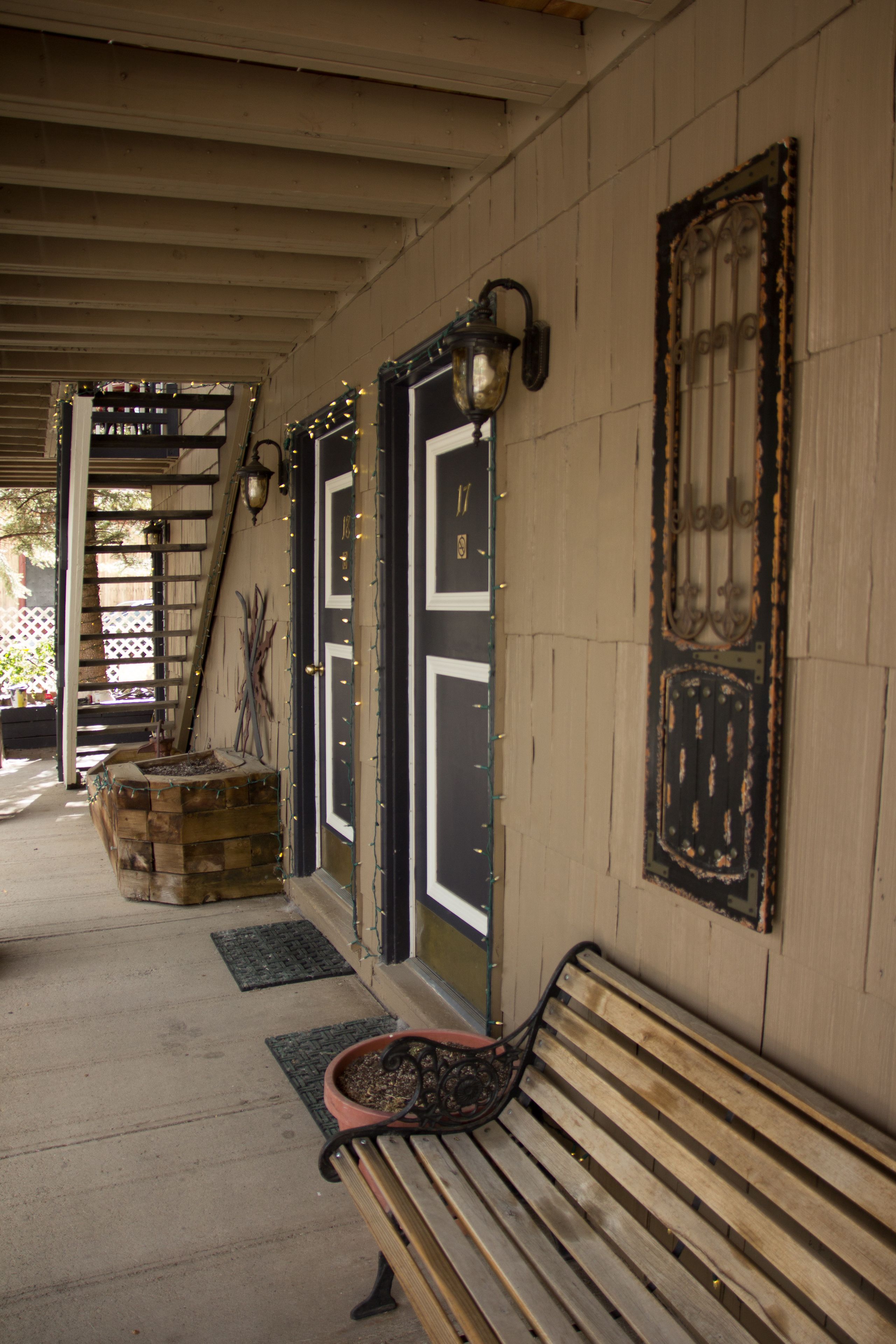 A covered outdoor area with a wooden bench, a potted plant, and decorative wall sconces.