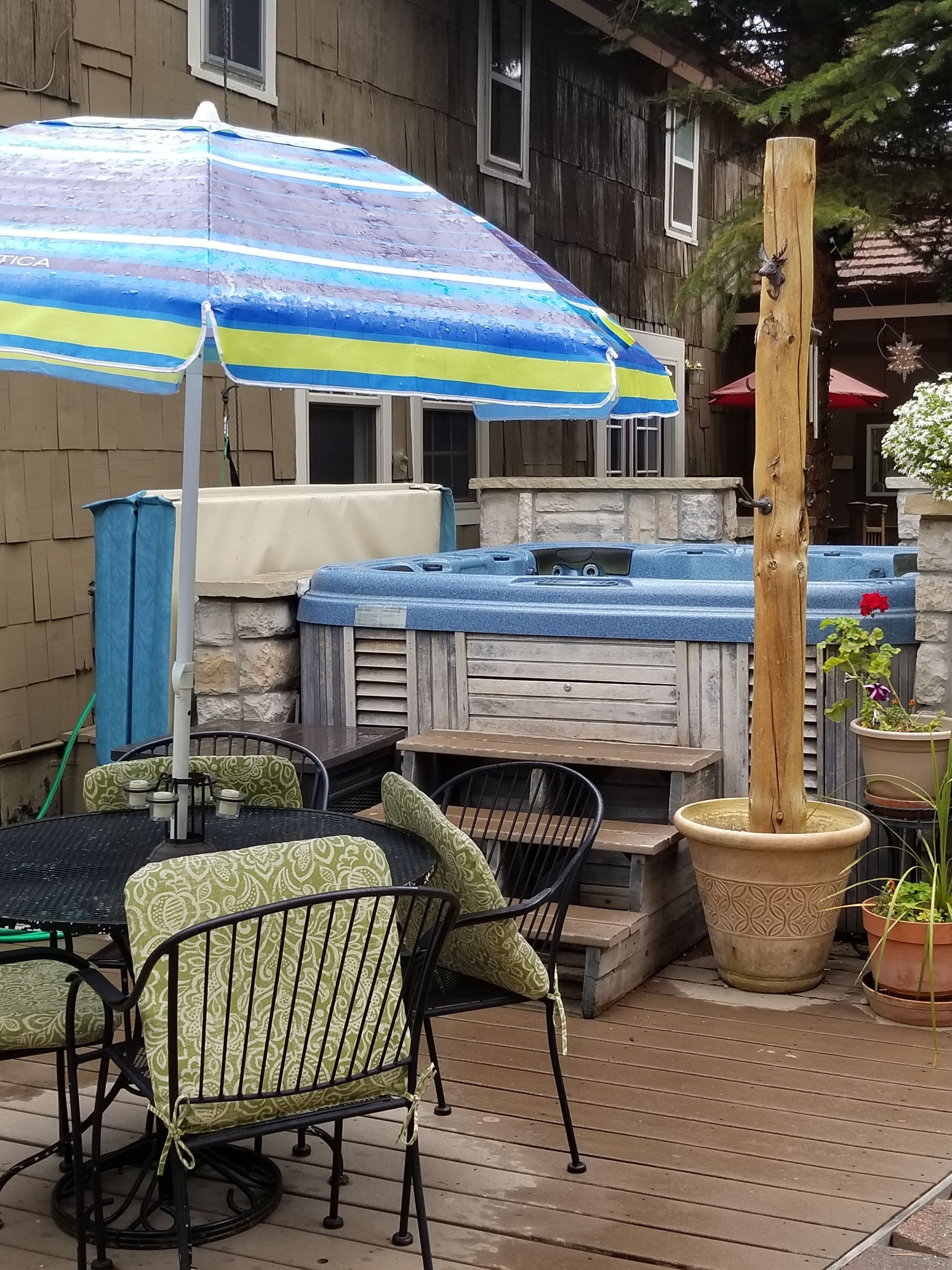 Una terrazza all'aperto con vasca idromassaggio, un tavolo di legno con sedie e un grande ombrellone a righe.