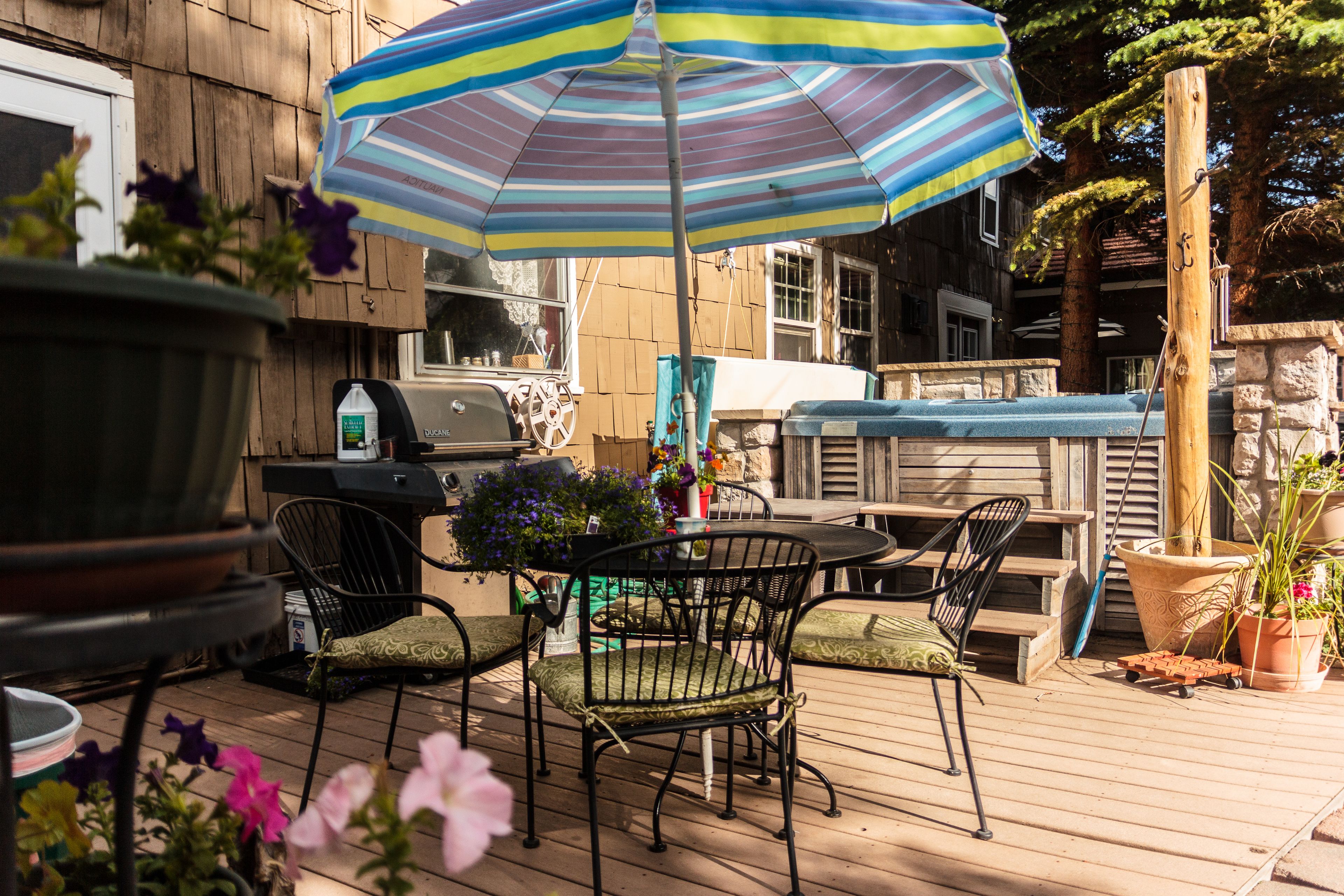A wooden deck with outdoor furniture, a grill, and a striped umbrella.