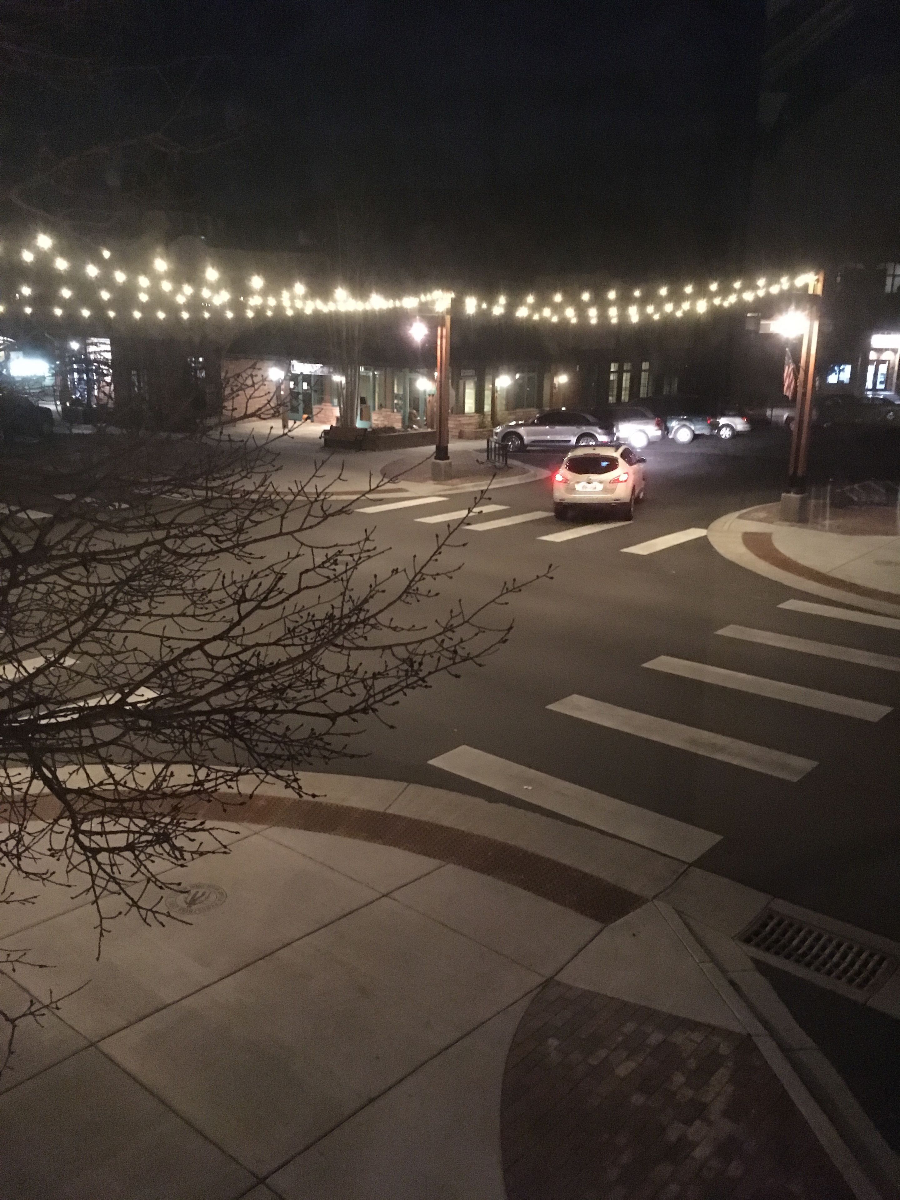 Nachtansicht einer Straße mit Fußgängerüberweg, Fahrzeugen und Lichterketten darüber.