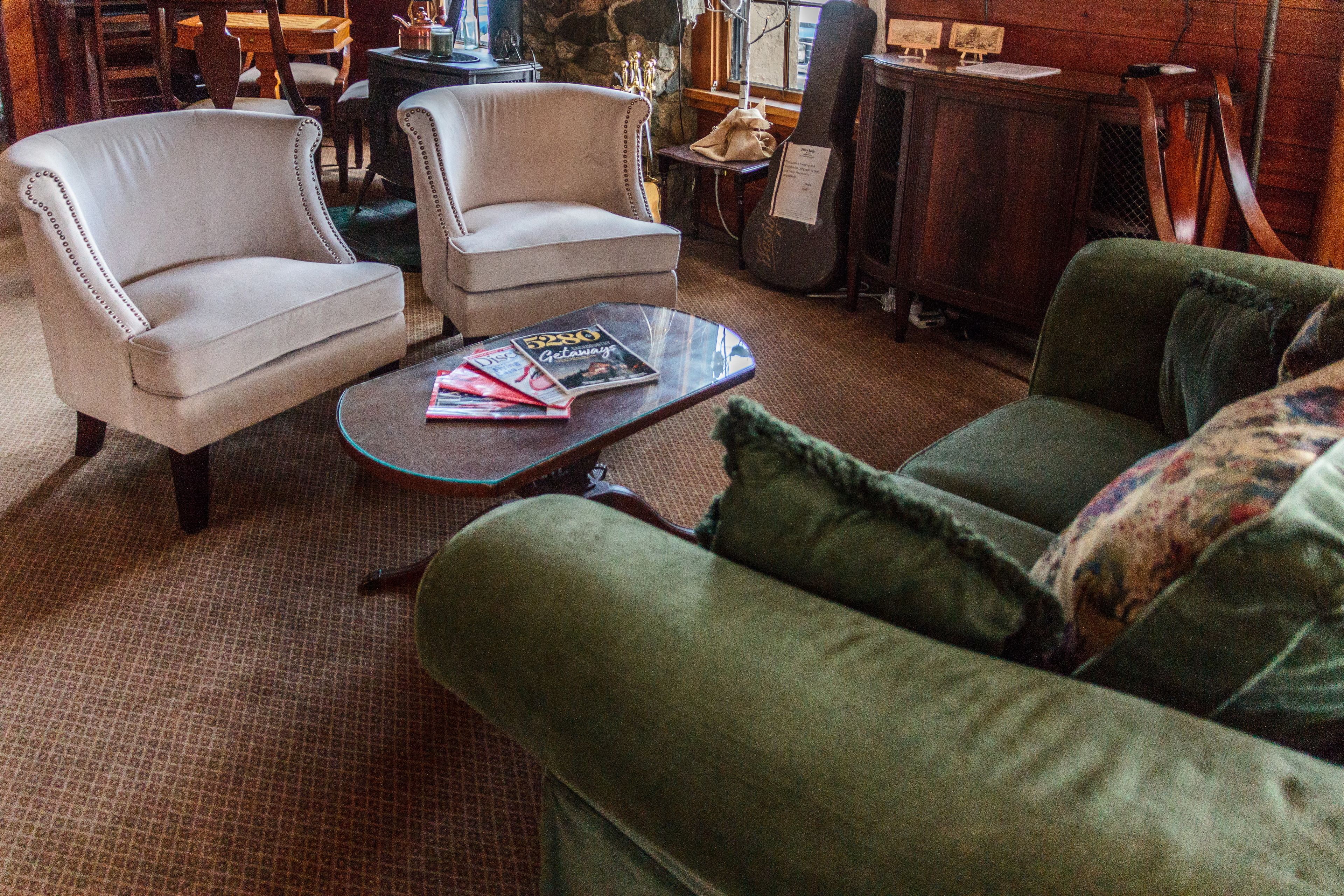 A cozy living room with a green sofa, two armchairs, a coffee table with magazines, and a guitar.