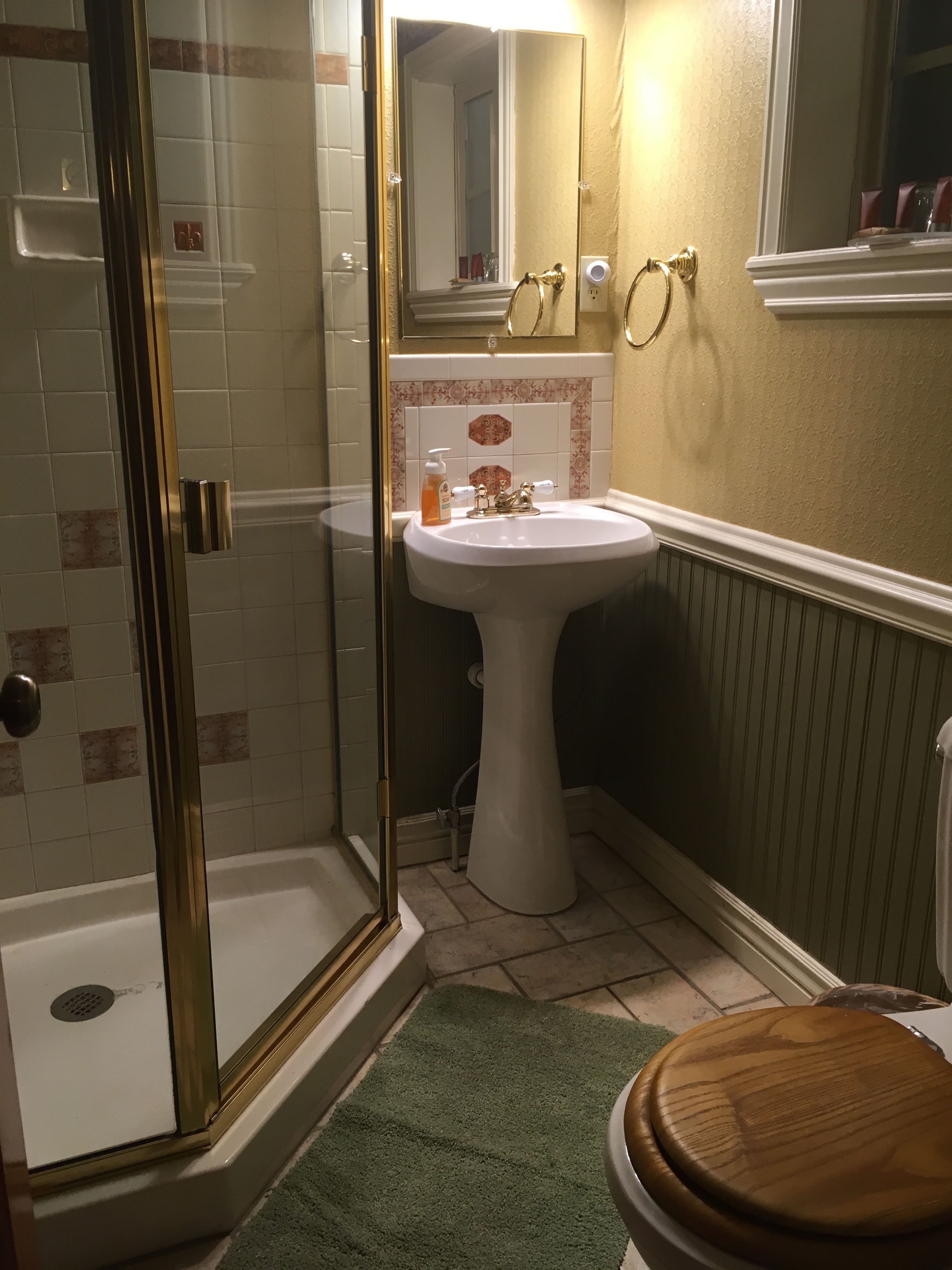 A bathroom with a glass-enclosed shower, a pedestal sink, and a wooden toilet.