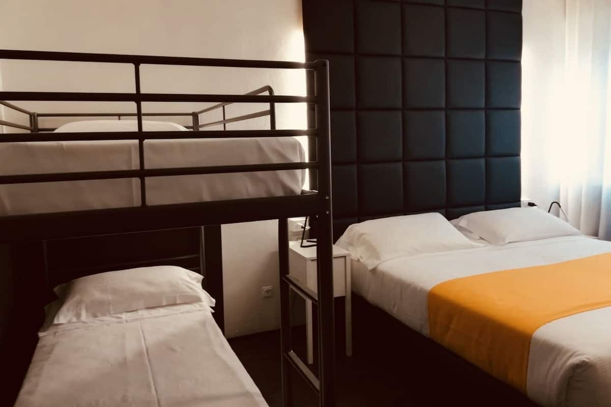 Una habitación de hotel con una litera, una cama individual, una mesita de noche y un cabecero oscuro.