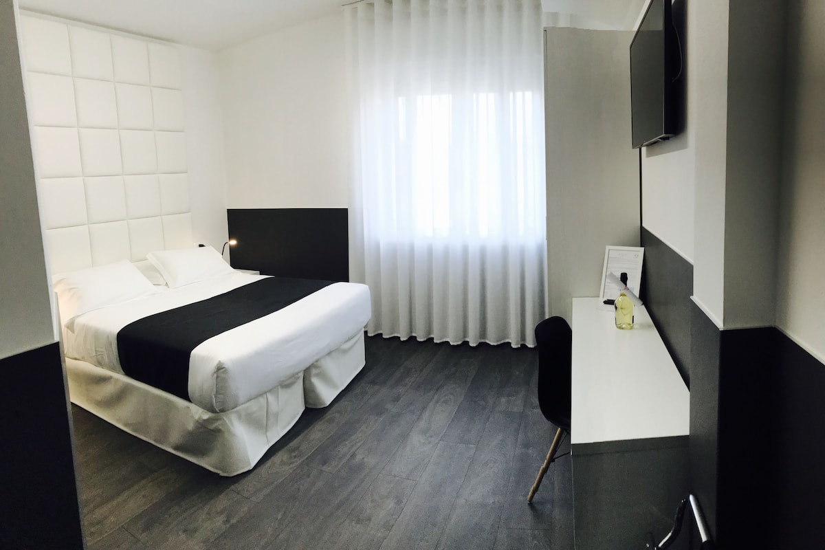 Habitación de hotel con cama, escritorio, silla, televisor de pantalla plana y ventana con cortinas.