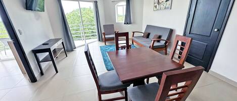 A modern living room with a dining table, chairs, a sofa, and a TV mounted on the wall.
