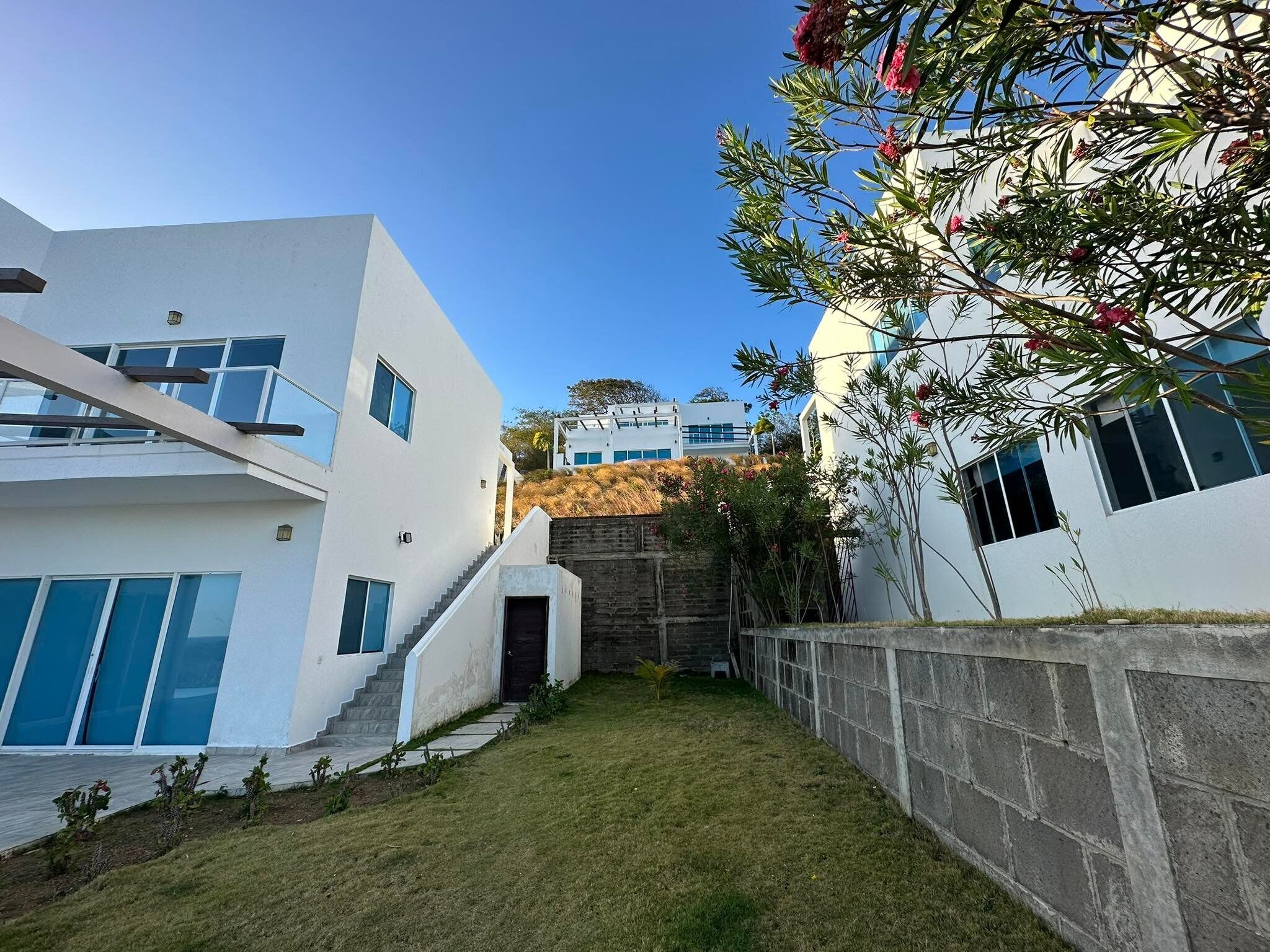 A modern building with a white facade, a stone retaining wall, and a grassy courtyard.