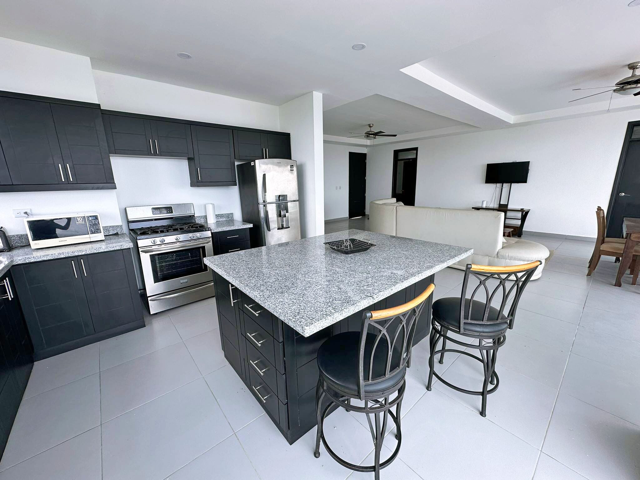 A modern kitchen with dark cabinets, stainless steel appliances, a granite countertop, and a bar area with stools.