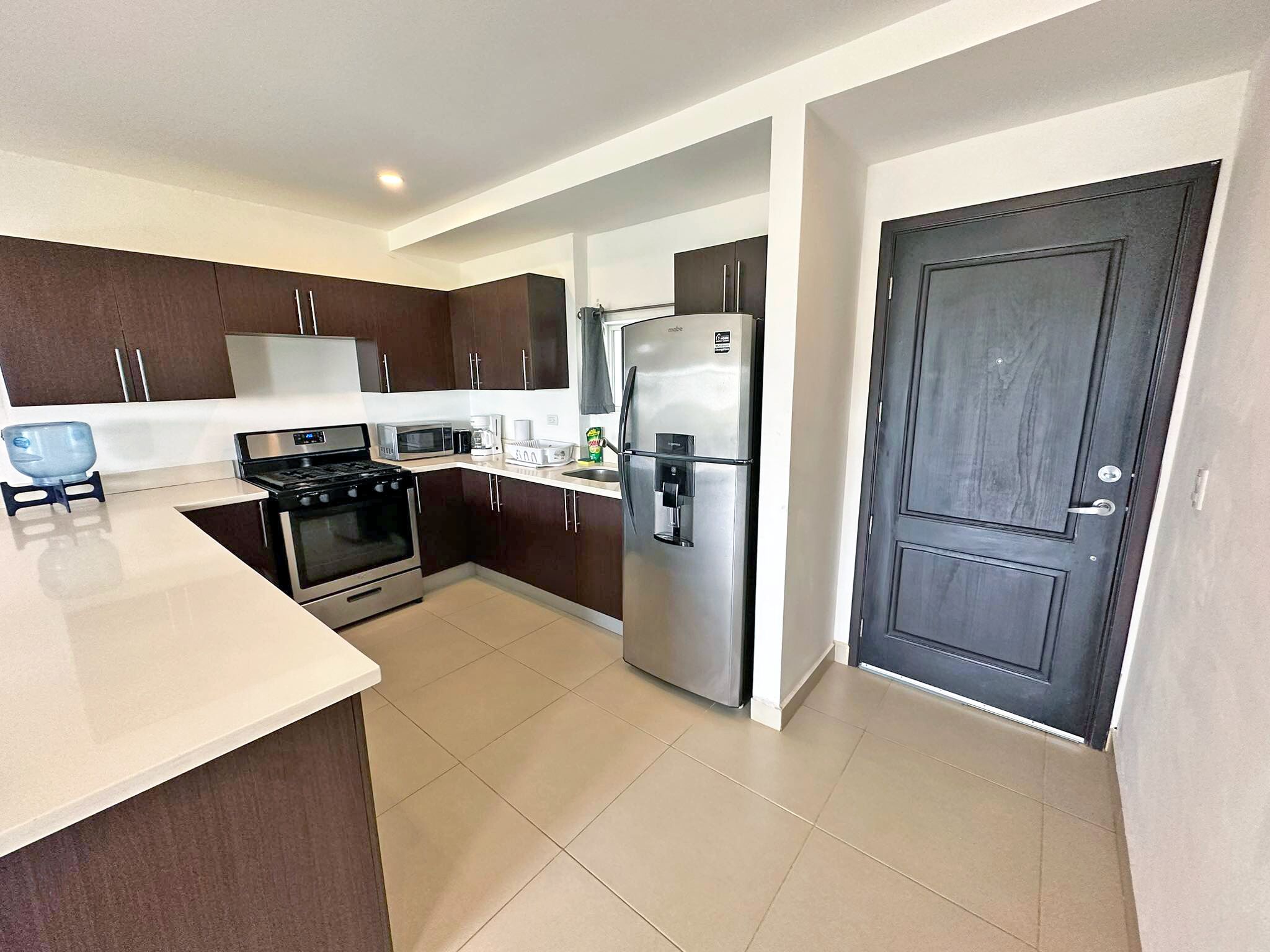 A modern kitchen with dark brown cabinets, a stainless steel refrigerator, a microwave, a stove, and a sink.