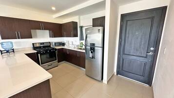 A modern kitchen with dark brown cabinets, a stainless steel refrigerator, a microwave, a stove, and a sink.