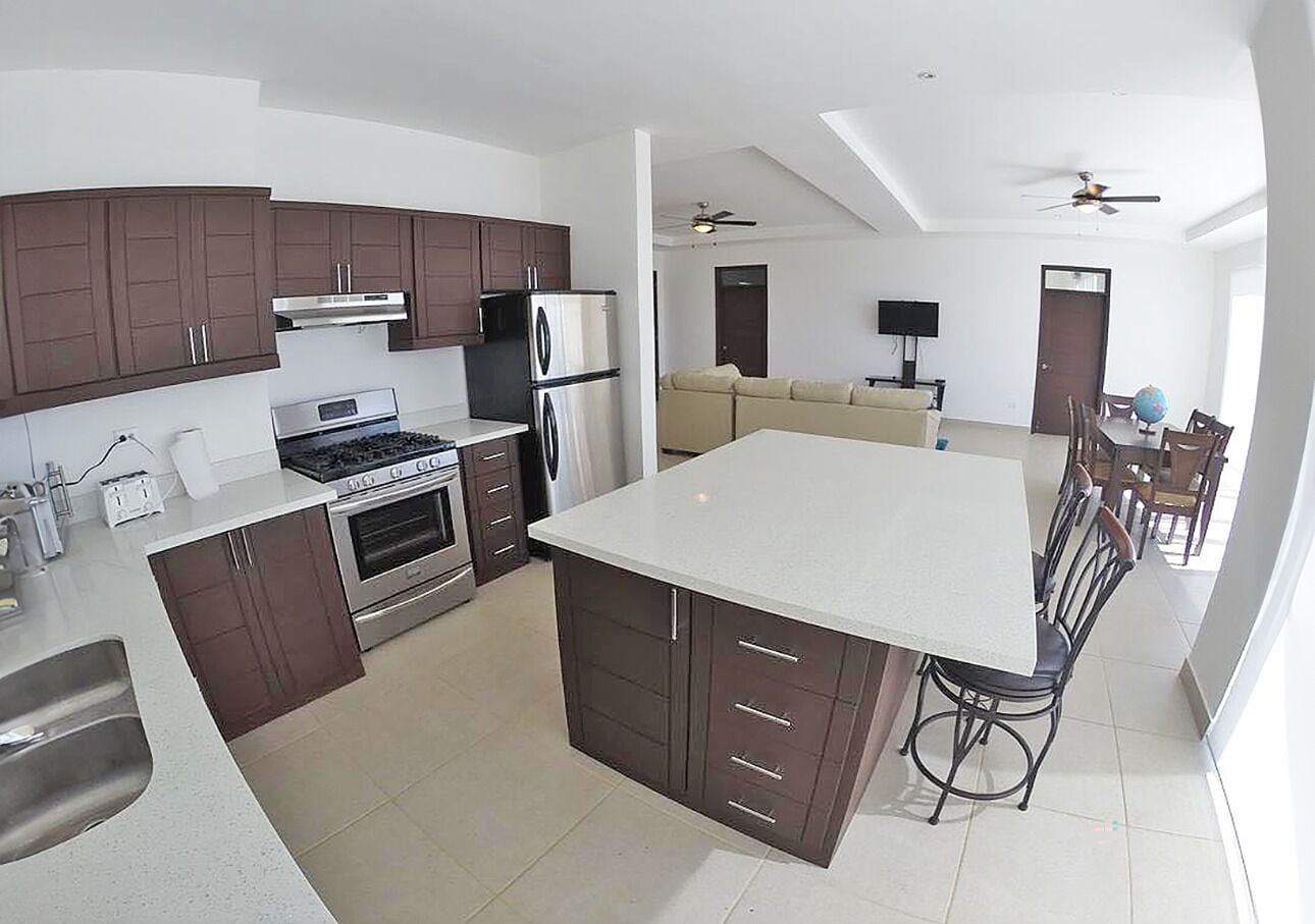 A modern kitchen with dark cabinets, stainless steel appliances, and a large island.
