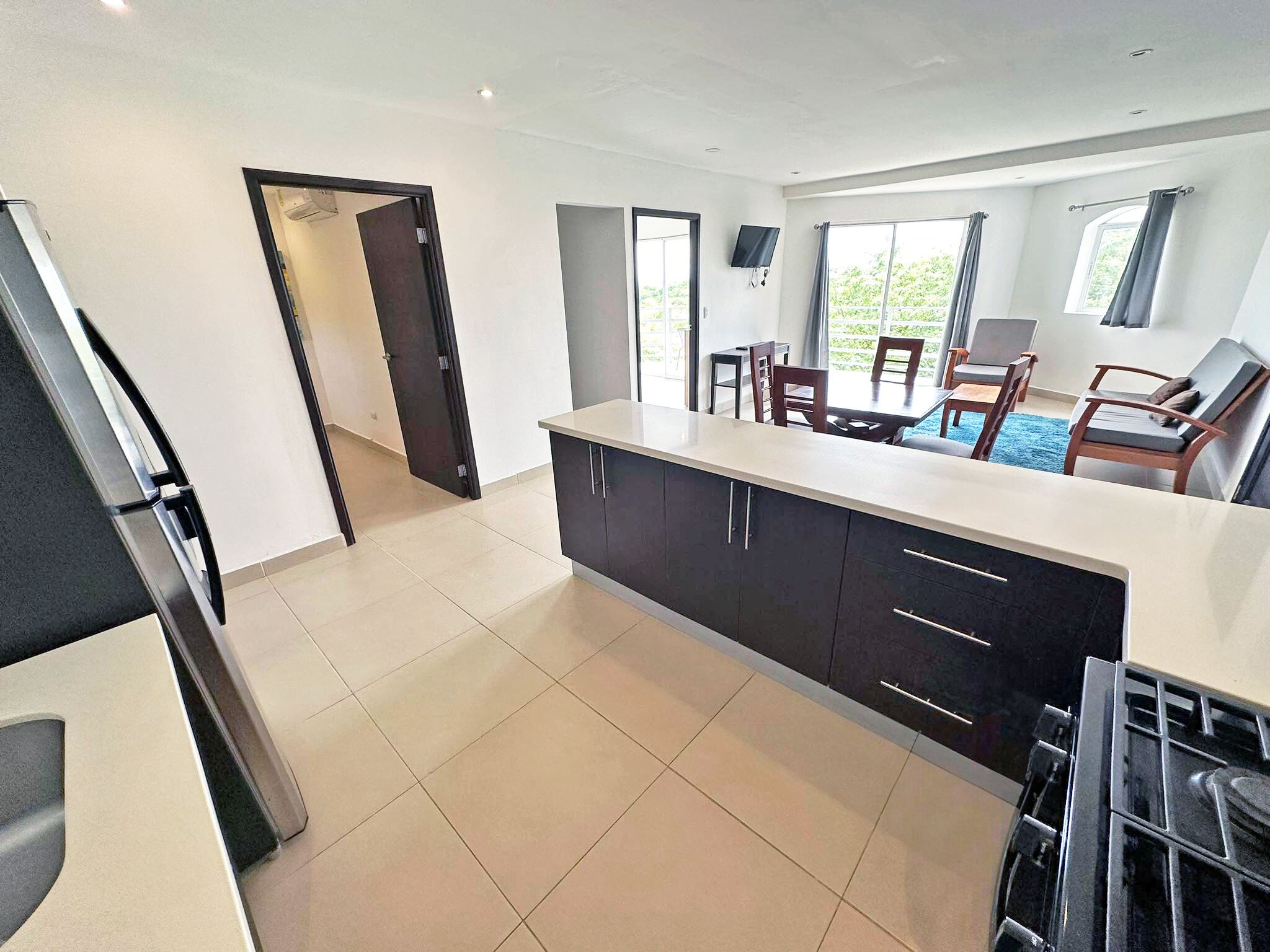 A modern kitchen with dark cabinets, a large island, and a dining area with chairs and a table.
