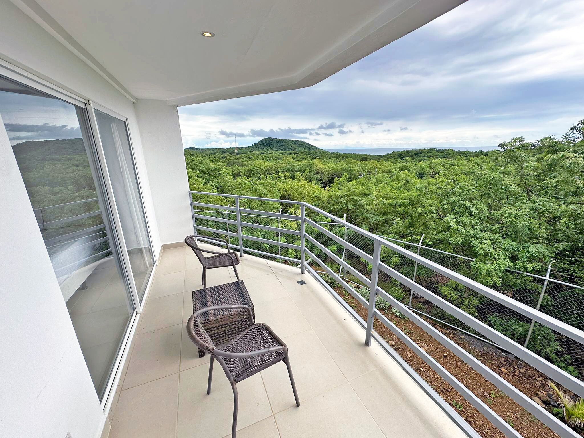 A balcony with two wicker chairs and a metal railing overlooking a lush green landscape.