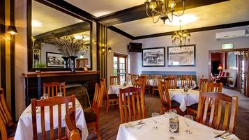 A dining area with wooden chairs and tables, a chandelier, and framed pictures on the walls.
