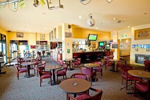 A bar area with multiple tables and chairs, a television screen, and a fireplace. - Katoomba Hotel (Katoomba)