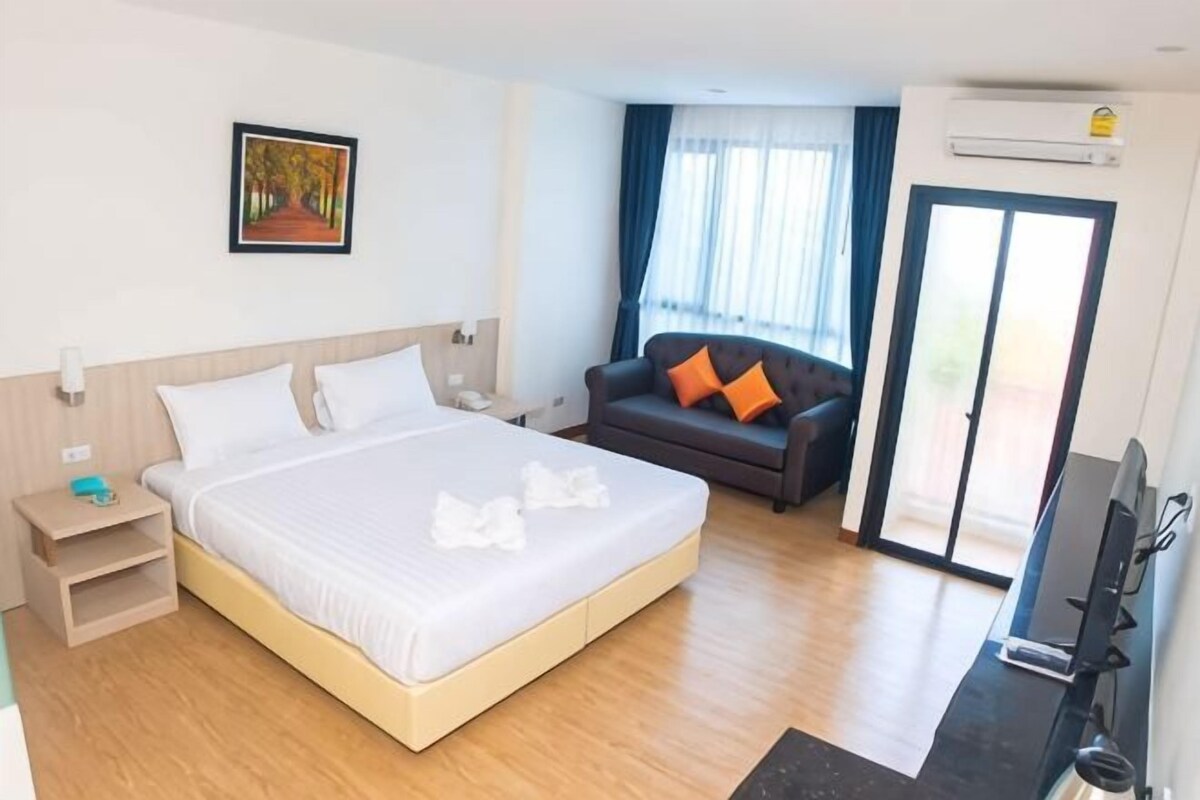 A hotel room with a large bed, a sofa, a TV, and a sliding glass door to the outside.