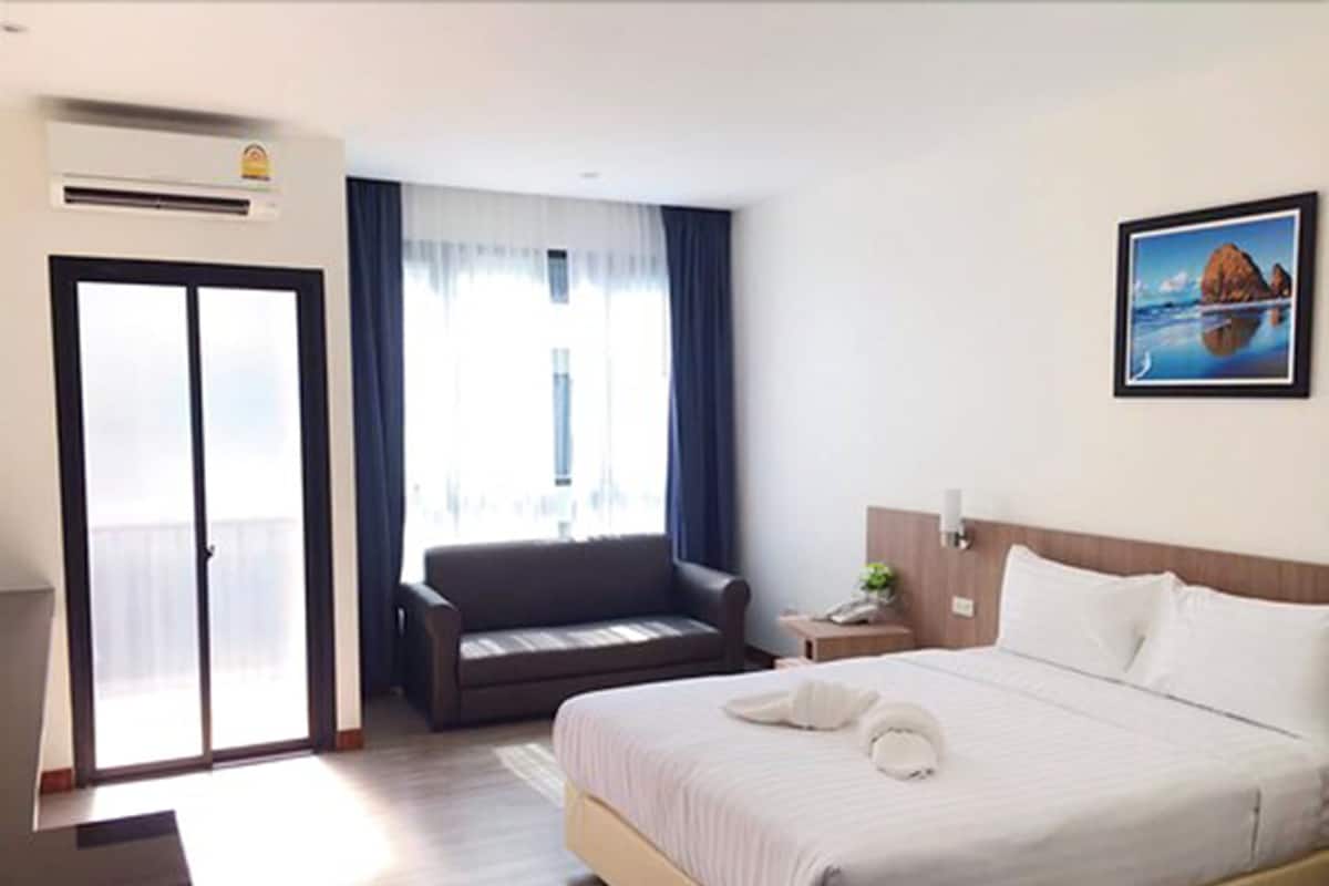 A hotel room with a bed, a sofa, a desk, and a window with curtains.