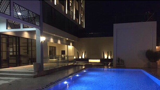 A modern outdoor pool area with a blue-lit water feature, surrounded by a building with large windows and a balcony. - Orchid Riverview Hotel (Surat Thani)