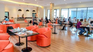 A modern dining area with orange chairs and tables, a central bar area, and large windows providing natural light. - Orchid Riverview Hotel (Surat Thani)