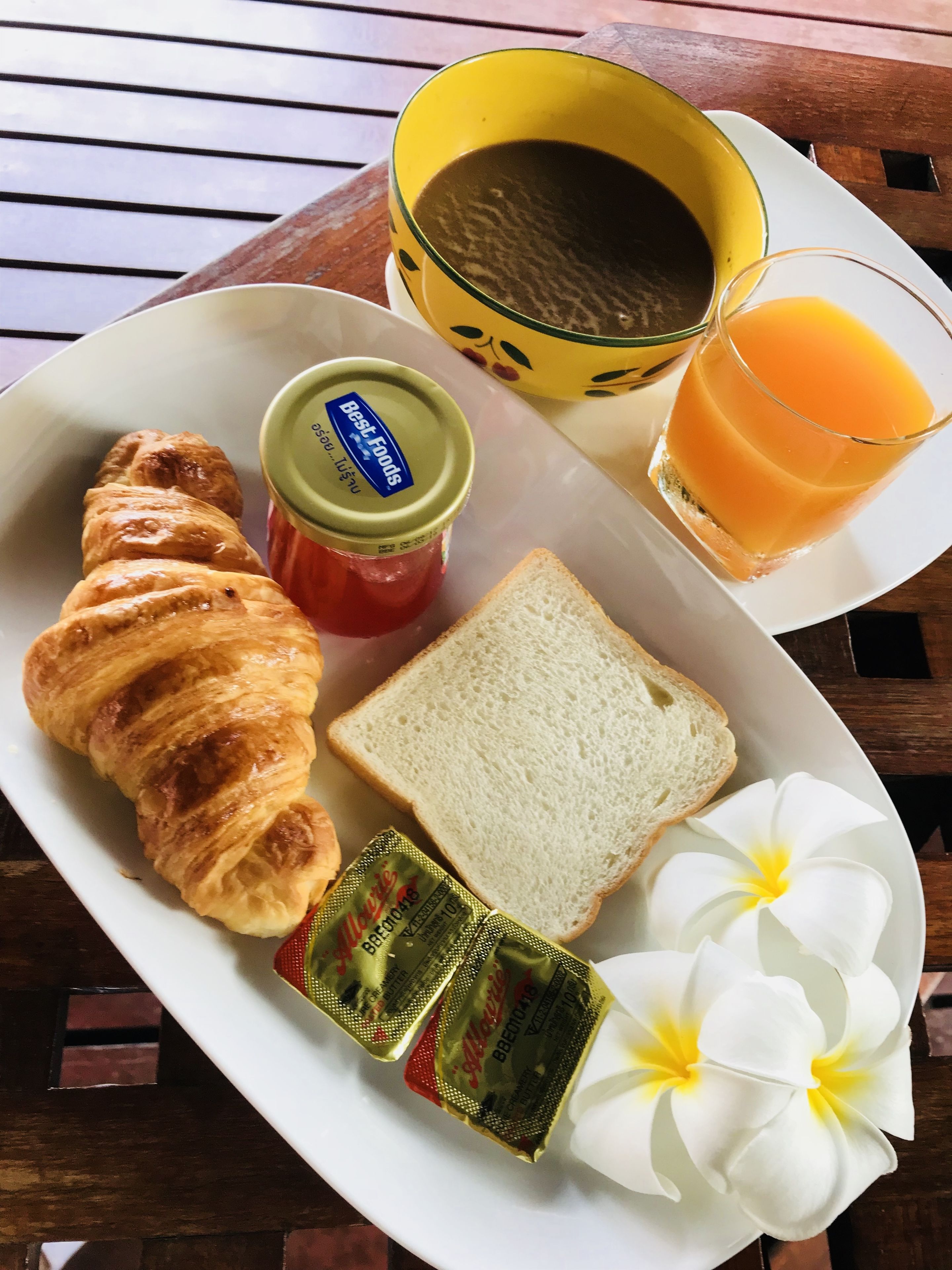 A breakfast tray with croissant, jam, butter, juice, and a flower.