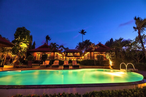 A resort with a swimming pool, lounge chairs, and palm trees.