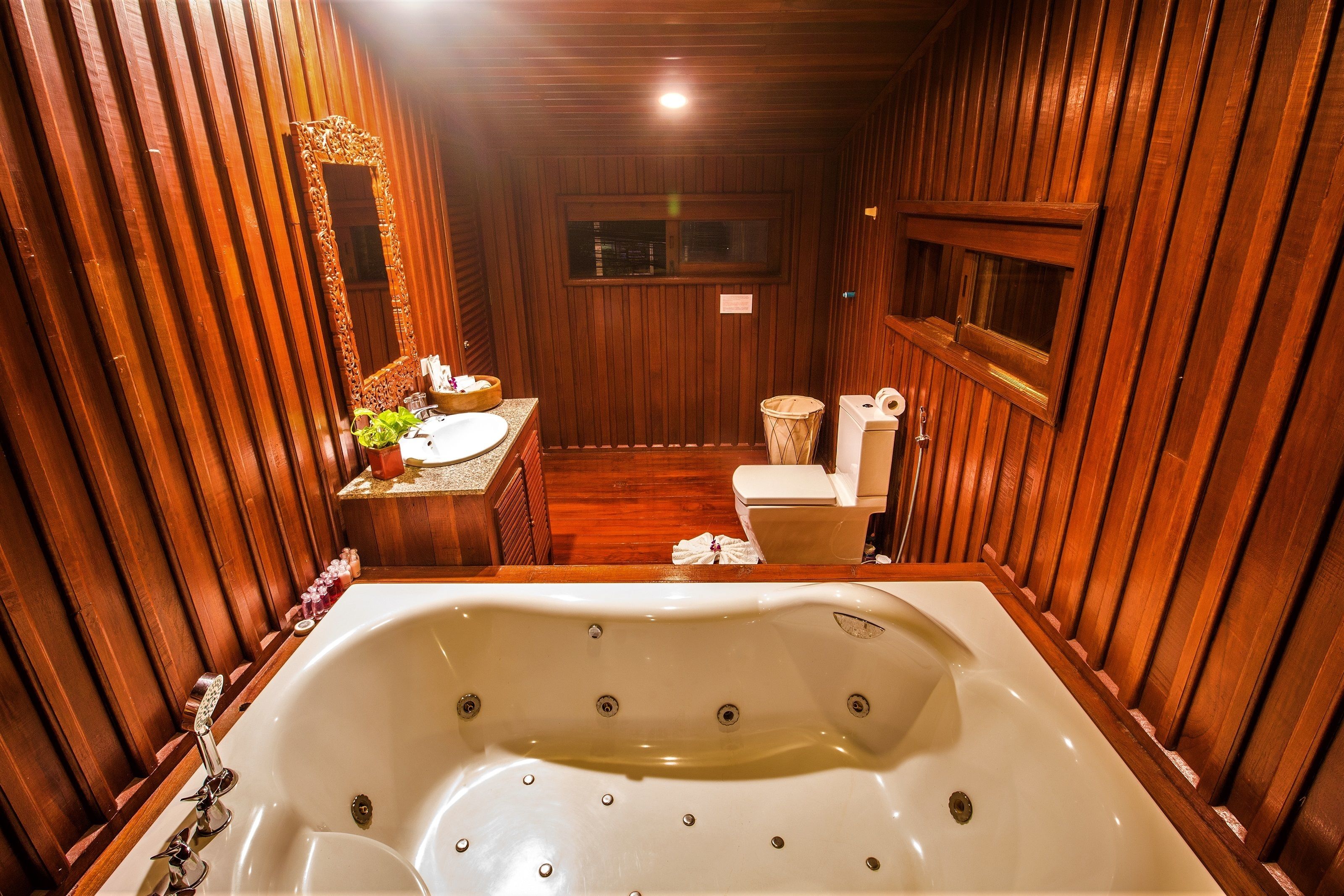 A wooden-paneled bathroom with a large bathtub, a sink, and a toilet.