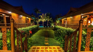 A traditional wooden building with a central pathway leading to a gate, surrounded by lush greenery and palm trees. - Erawan Villa Hotel (Koh Samui)