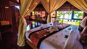 A spacious room with a large bed, a wooden floor, and a view of palm trees through the window. - Erawan Villa Hotel (Koh Samui)