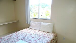 A small, simple bedroom with a single bed, a window with curtains, and a shelf. - Pousada Portal do Sol (Bombinhas)