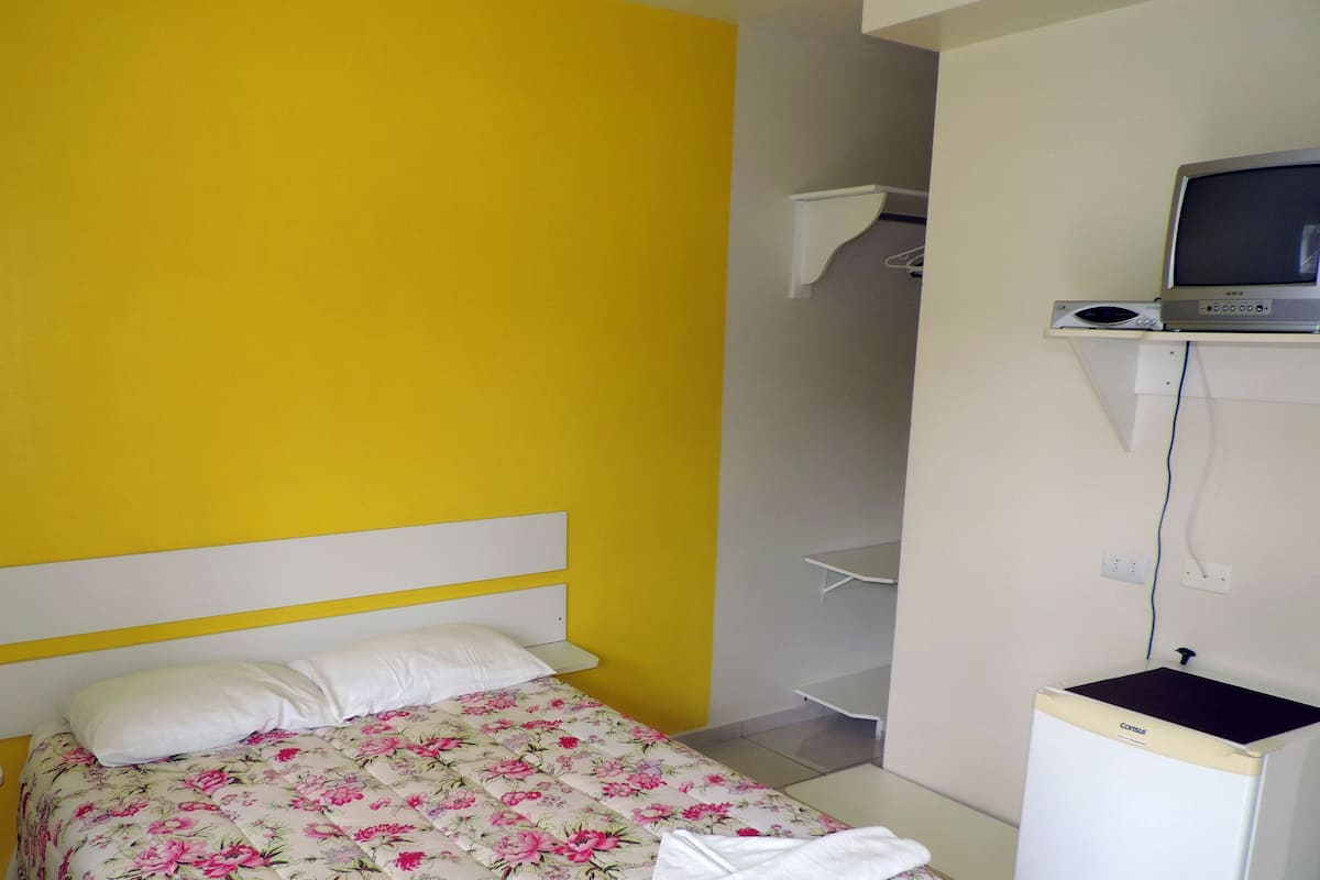 A room with a bed, a television on a stand, and a small cabinet.