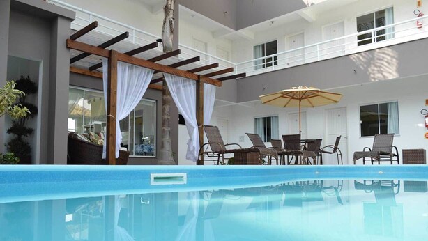 A pool area with a pergola, outdoor seating, and a view of the building's interior. - Pousada Portal do Sol (Bombinhas)