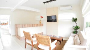 A bright living room with a white sofa, two wicker chairs, a coffee table, a TV, and a plant. - Pousada Portal do Sol (Bombinhas)