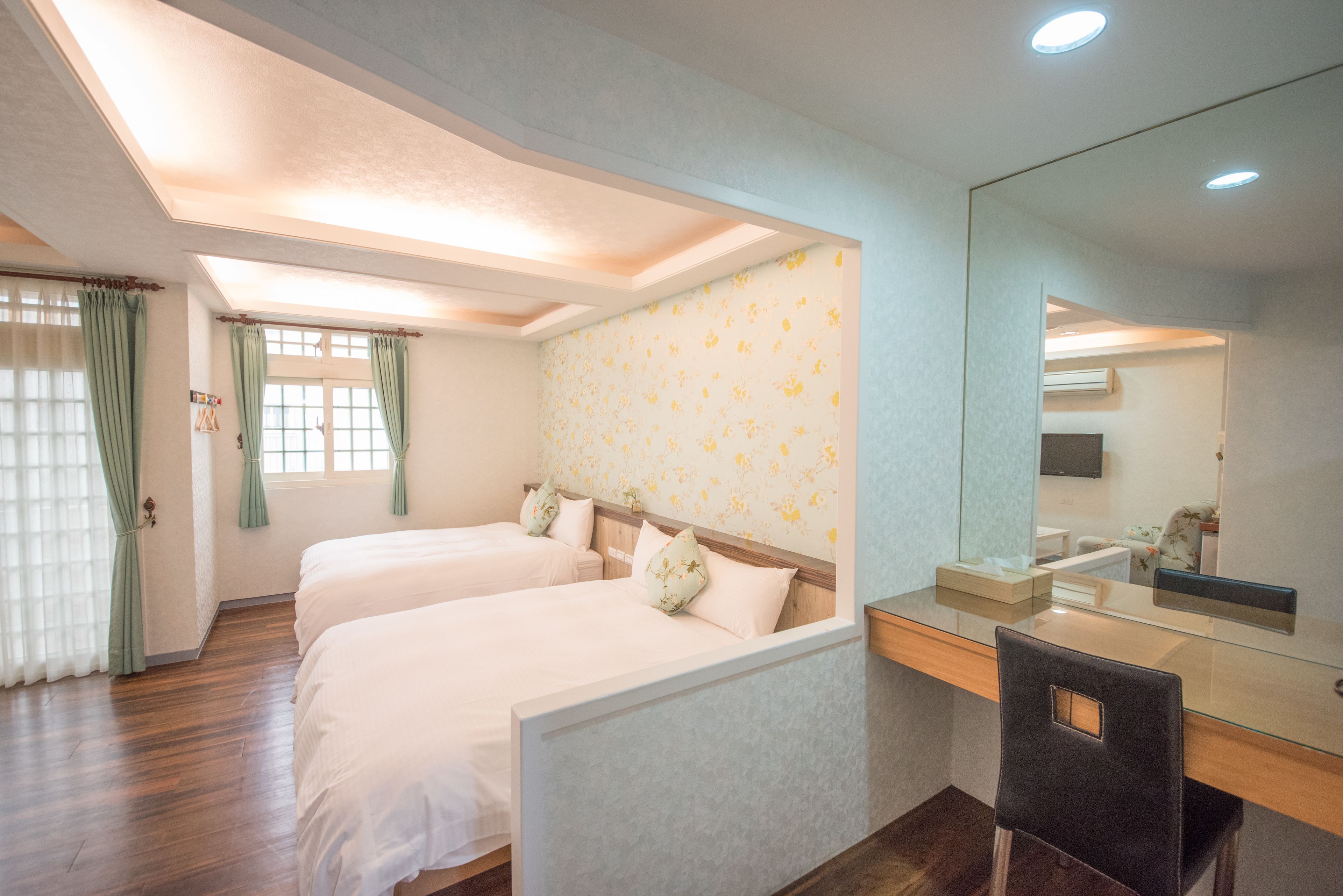 A hotel room with two beds, a desk, a chair, a mirror, and a window with curtains.