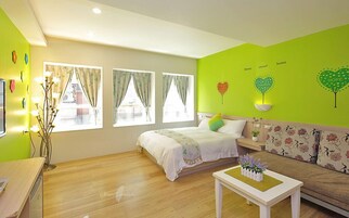 Una habitación luminosa con una cama, un sofá y una pequeña mesa. Hay tres ventanas con cortinas.