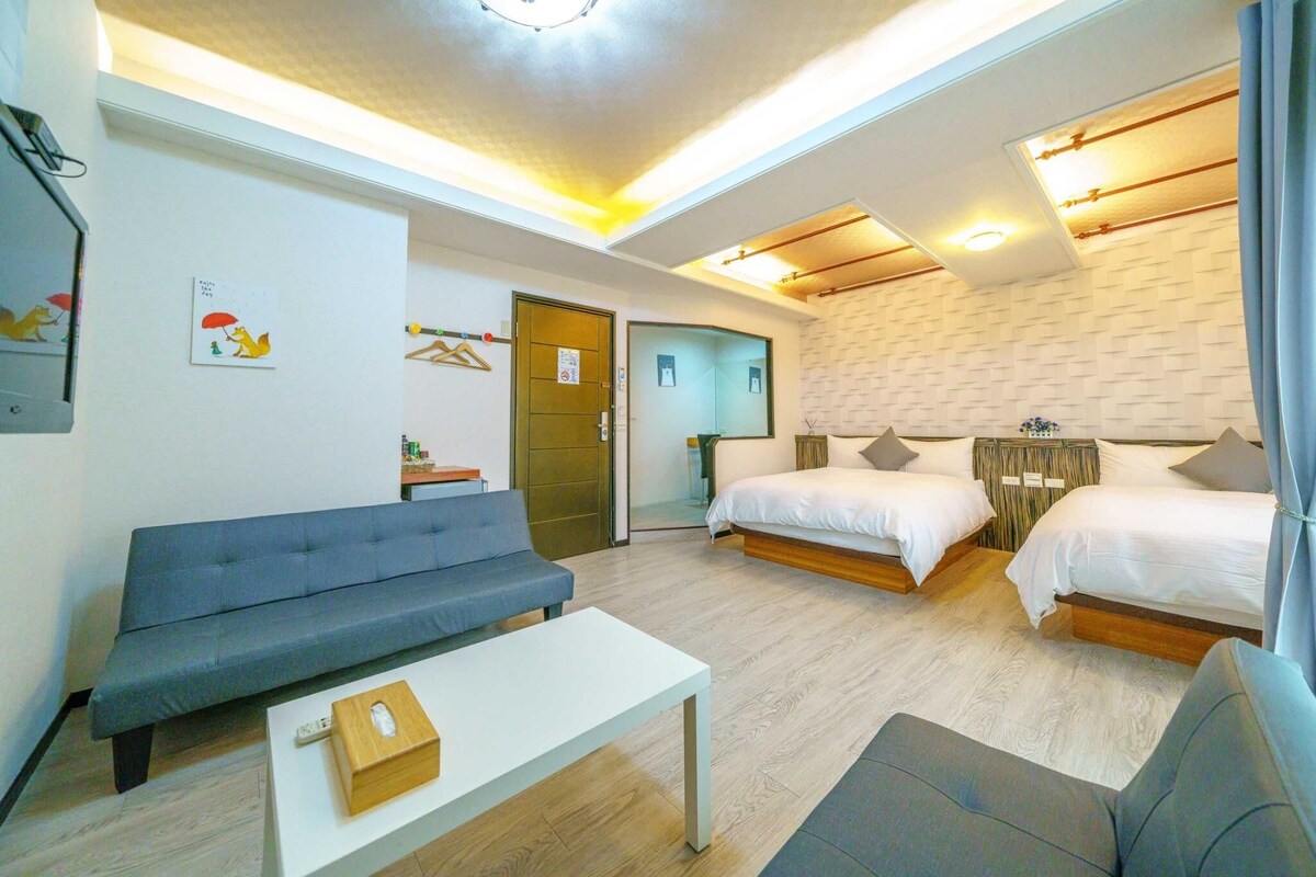 Een moderne hotelkamer met een bank, twee bedden, een tafeltje en een spiegel.