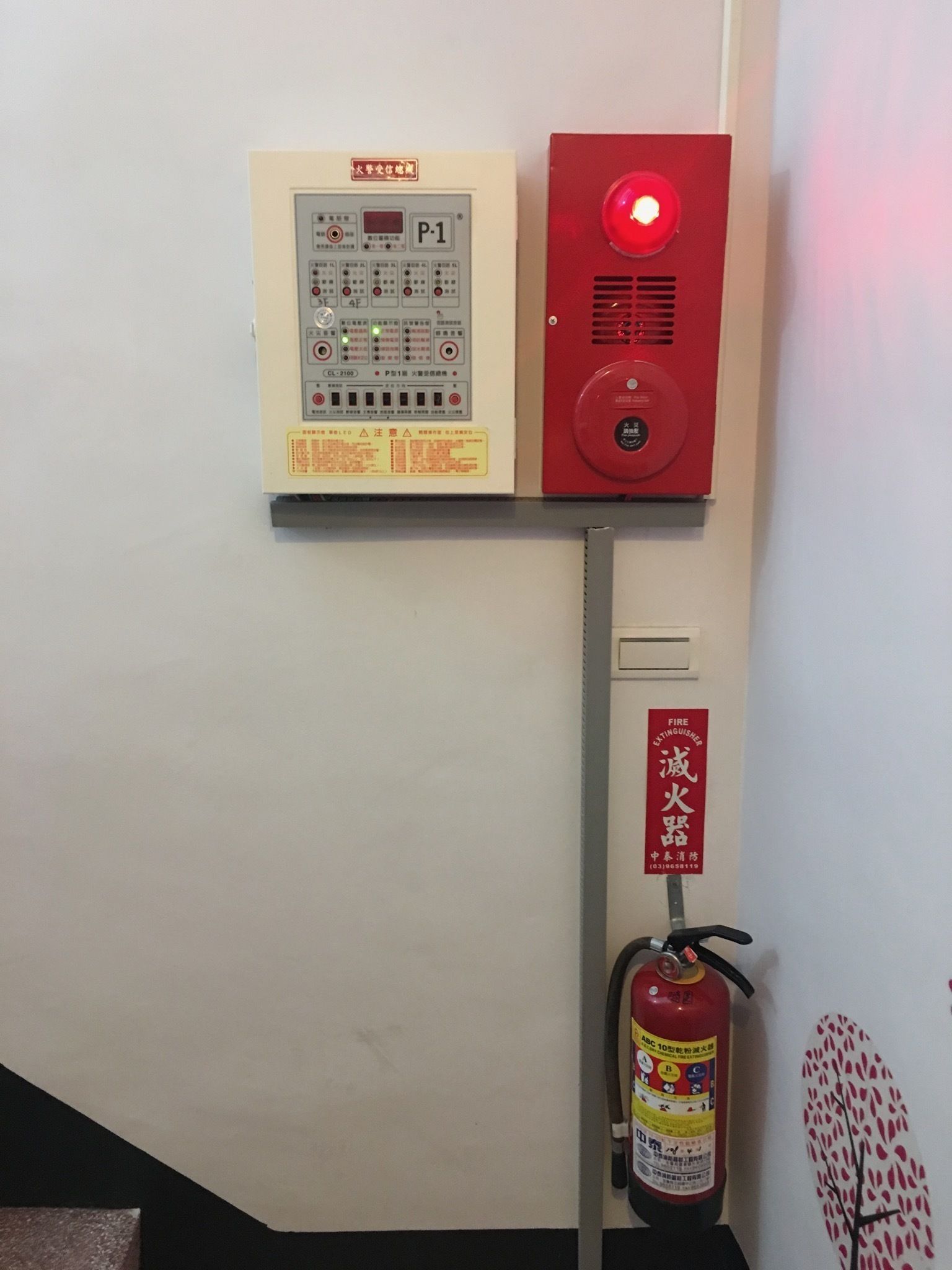 A fire alarm control panel and a fire extinguisher mounted on a wall.