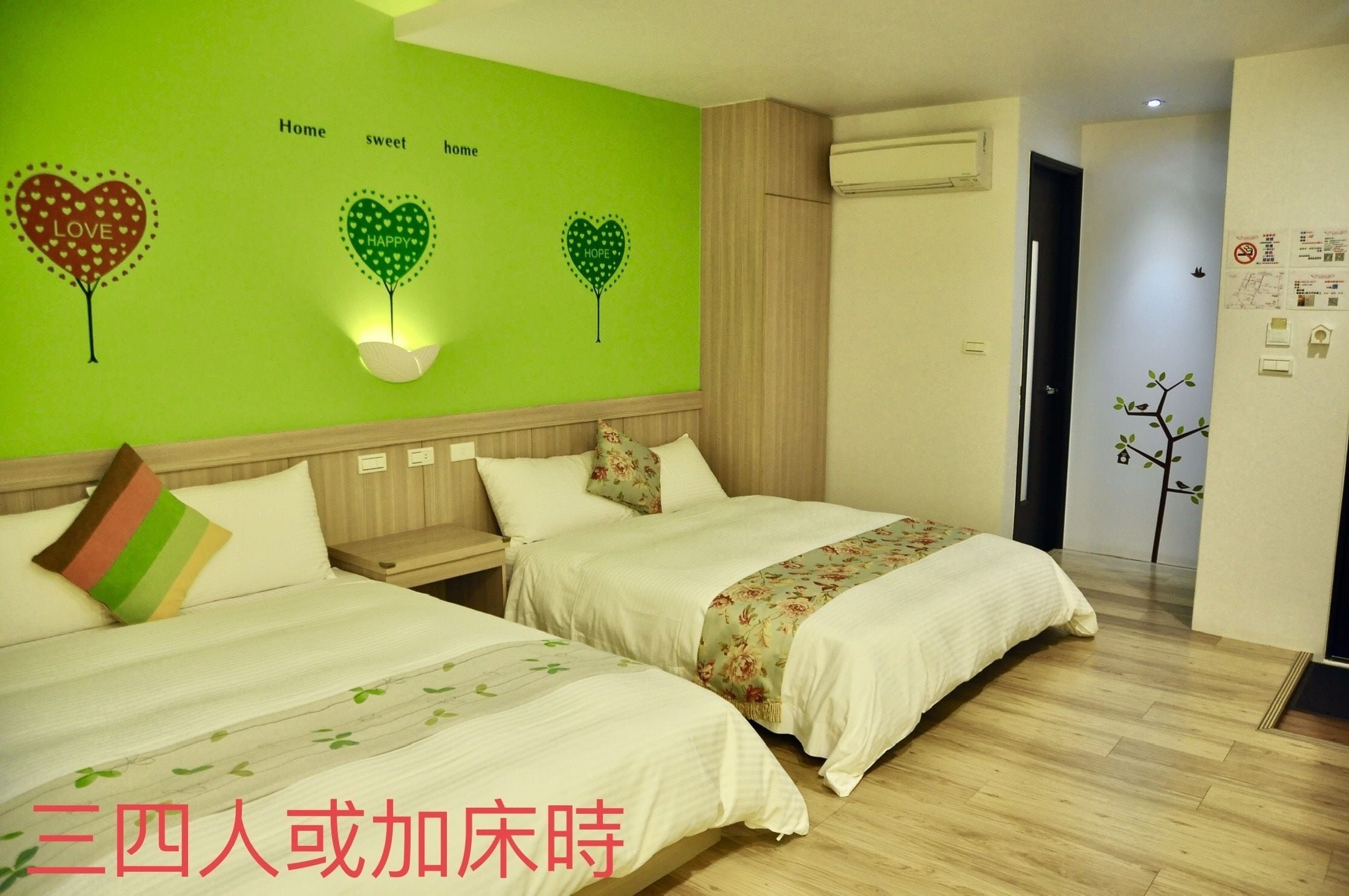 Habitación de hotel con dos camas, una pared verde decorada con corazones y suelo de madera.