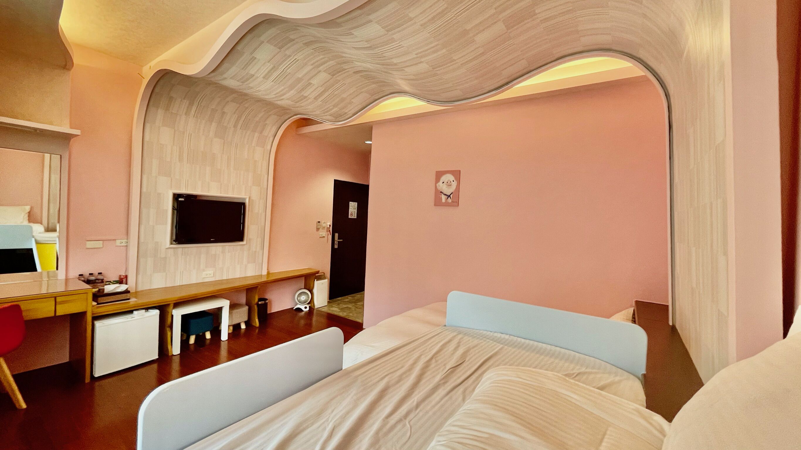 Een moderne hotelkamer met een opvallend golvend plafond, een bed met wit en blauw beddengoed, een bureau met computer en een flatscreen televisie aan de muur.