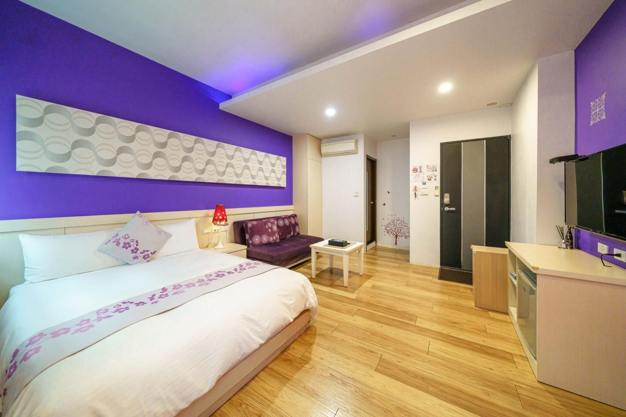 A modern hotel room with a bed, a small sofa, a desk, and a television.