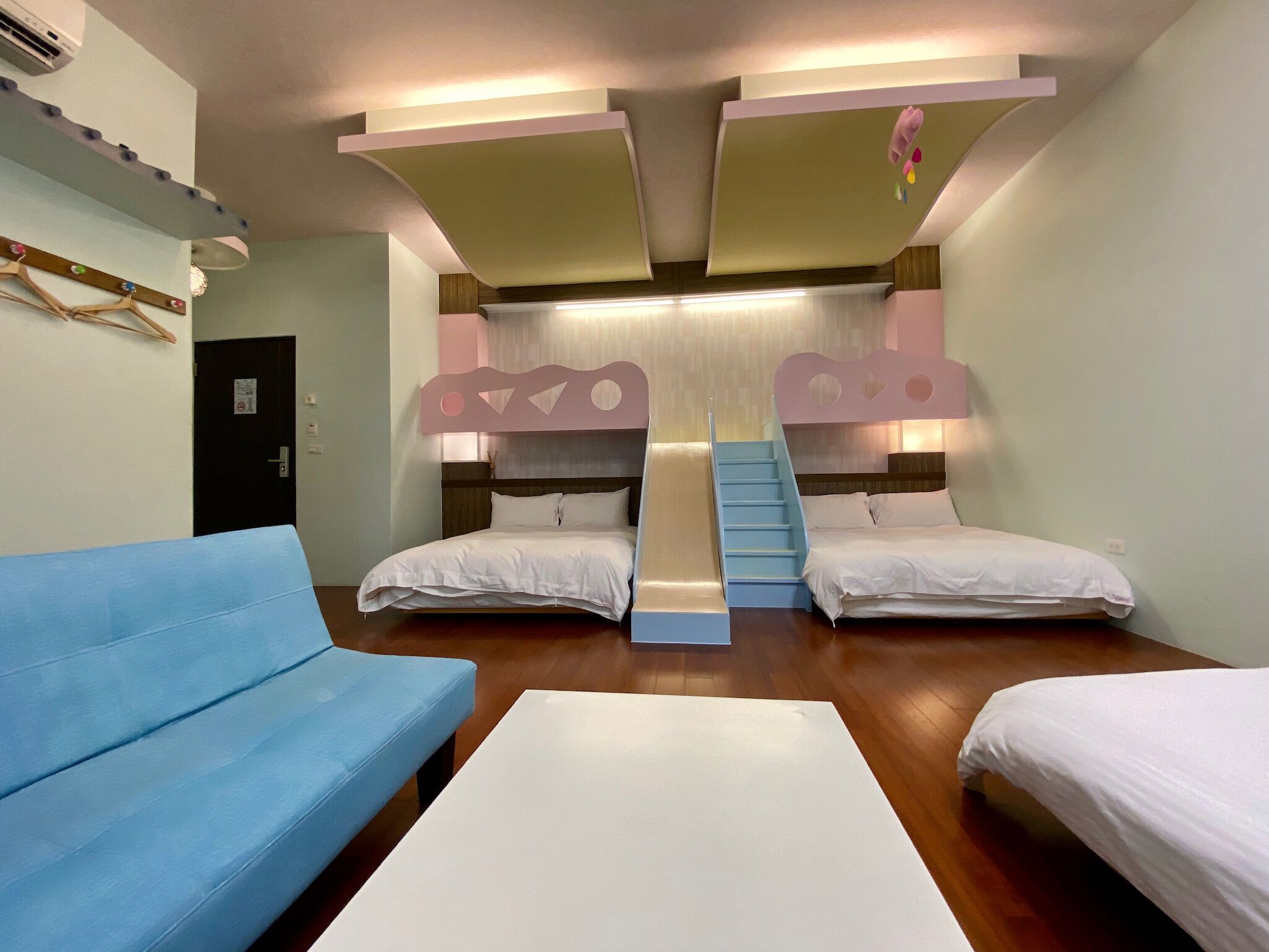 A room with two beds, a blue sofa, and a white table.