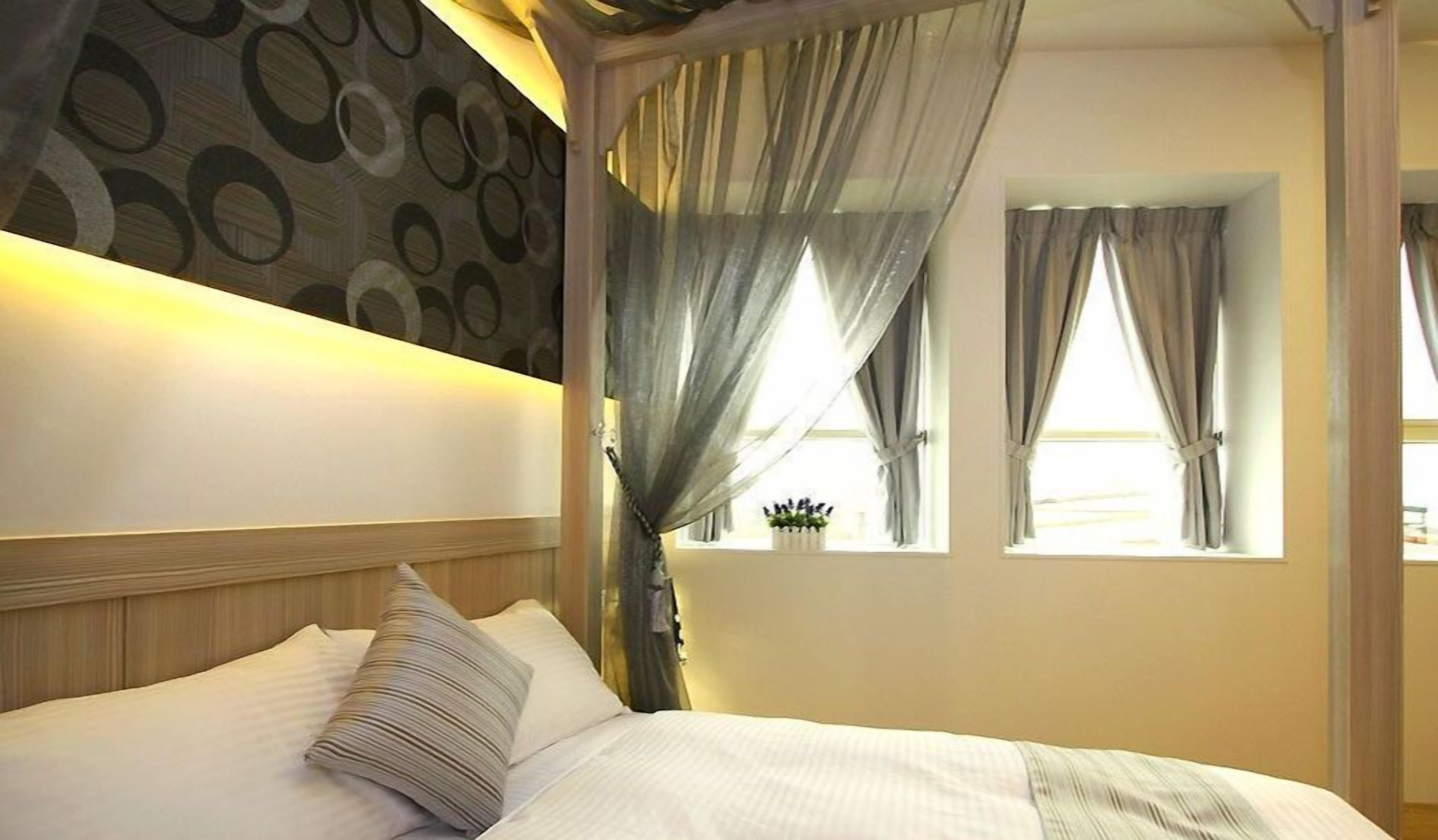 A hotel room with a bed, a wall with circular patterns, and two windows with curtains.