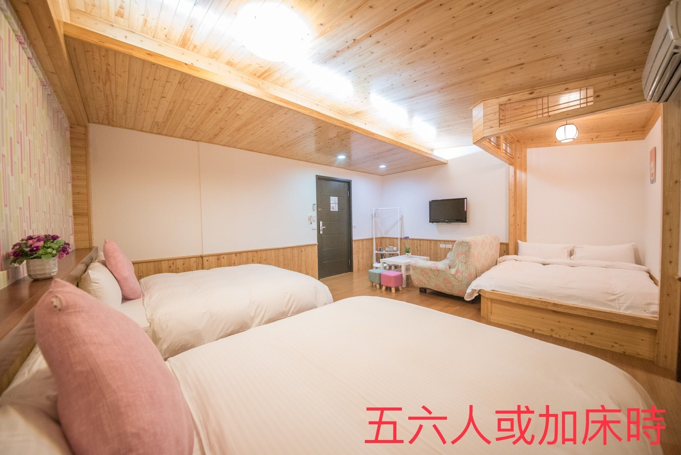 Una habitación con dos camas, techo de madera, una mesita con una silla y un televisor montado en la pared.