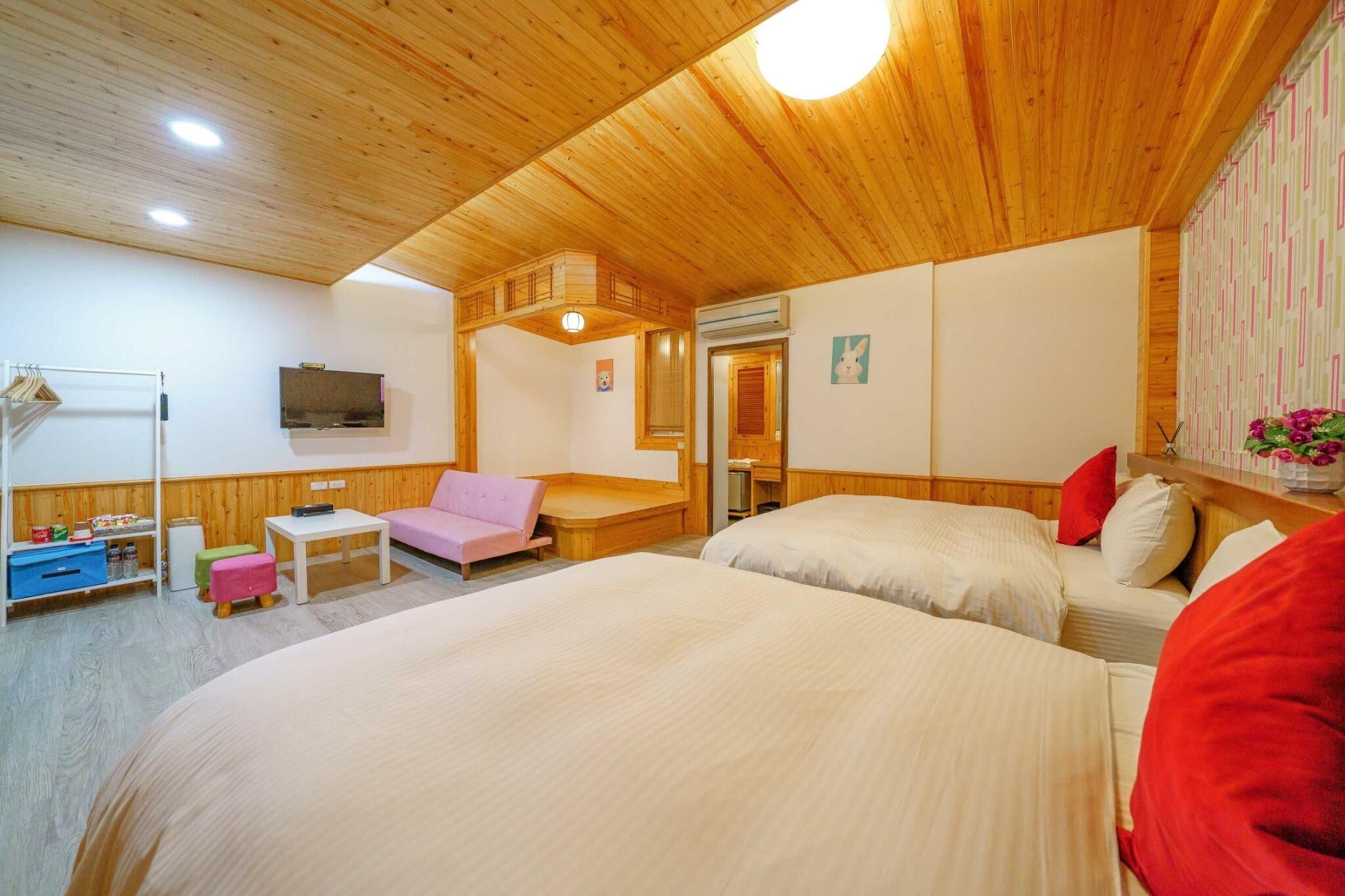 Um quarto aconchegante com tetos de madeira, duas camas, uma cadeira rosa e uma pequena mesa.