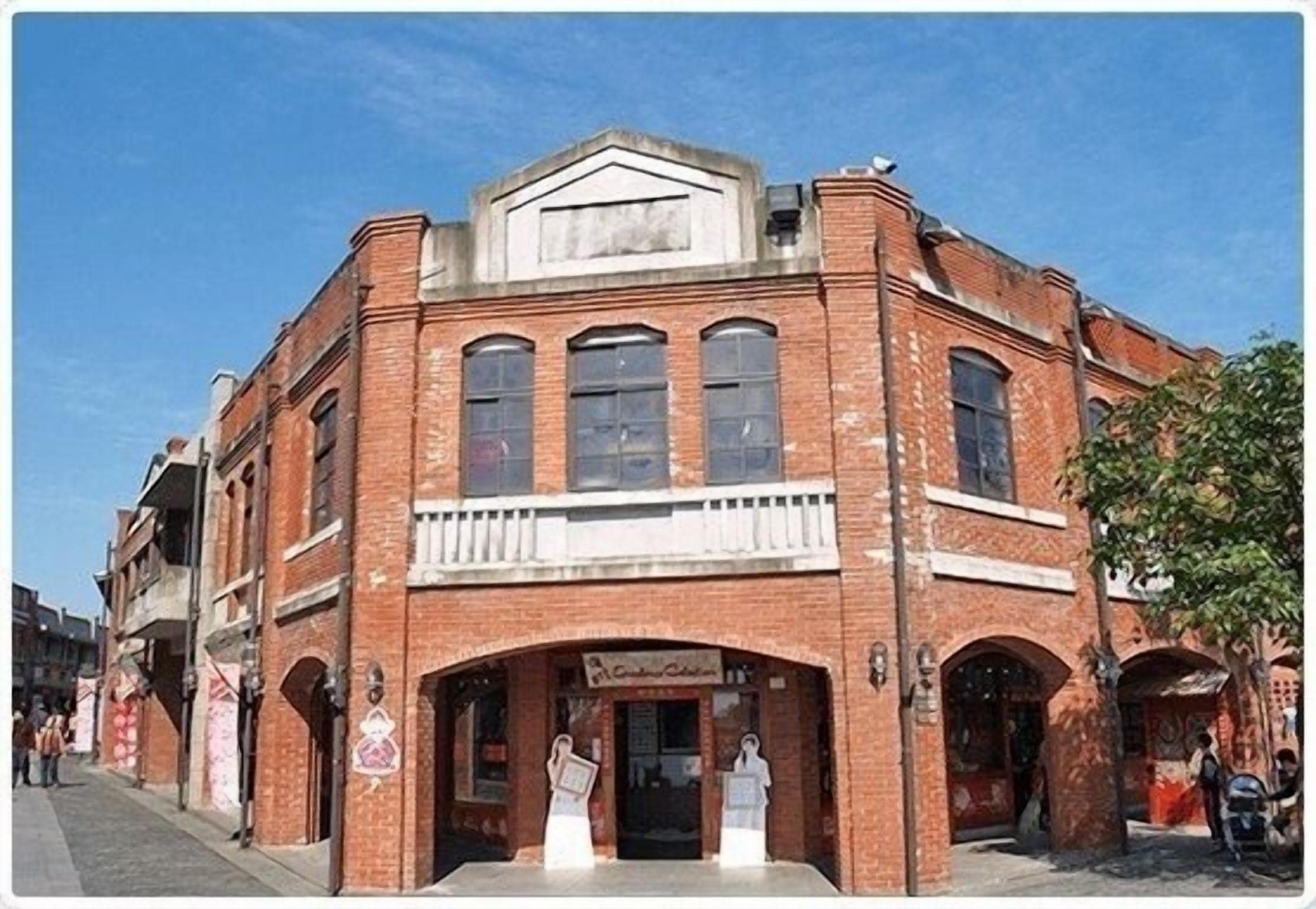 A historic brick building with a central entrance, large windows, and a balcony.