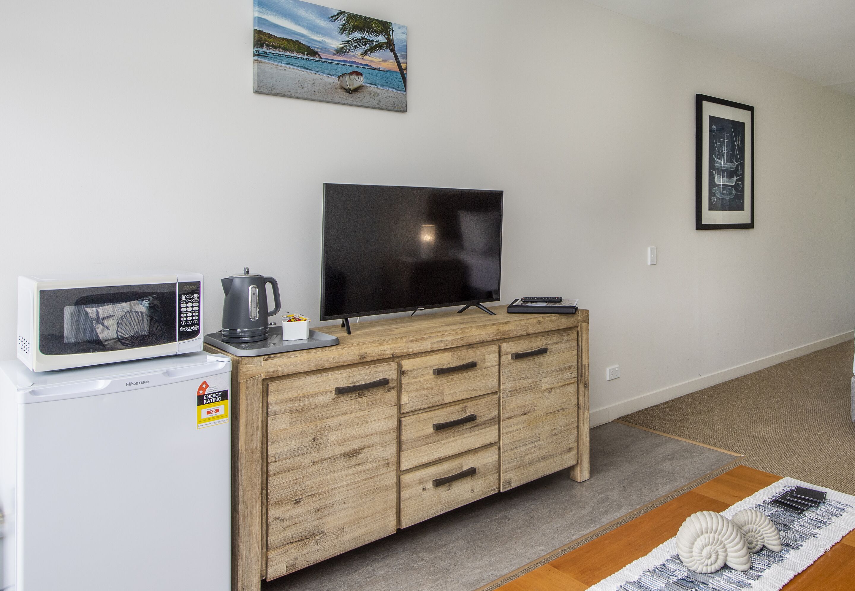 A compact living space with a kitchenette, a flat-screen TV, wooden cabinetry, and a small rug.