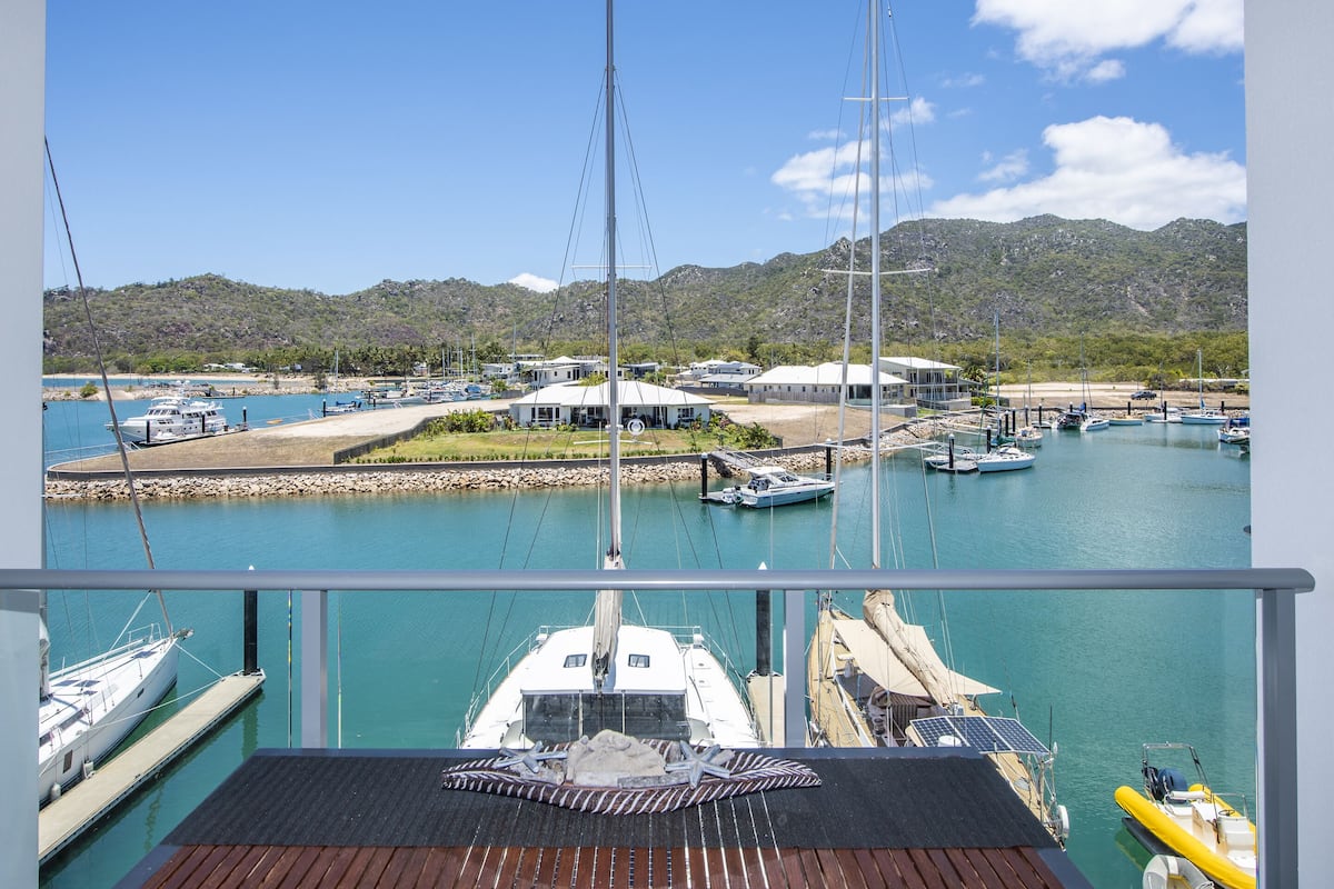 A marina with boats docked, a building with a white roof, and a mountainous backdrop.