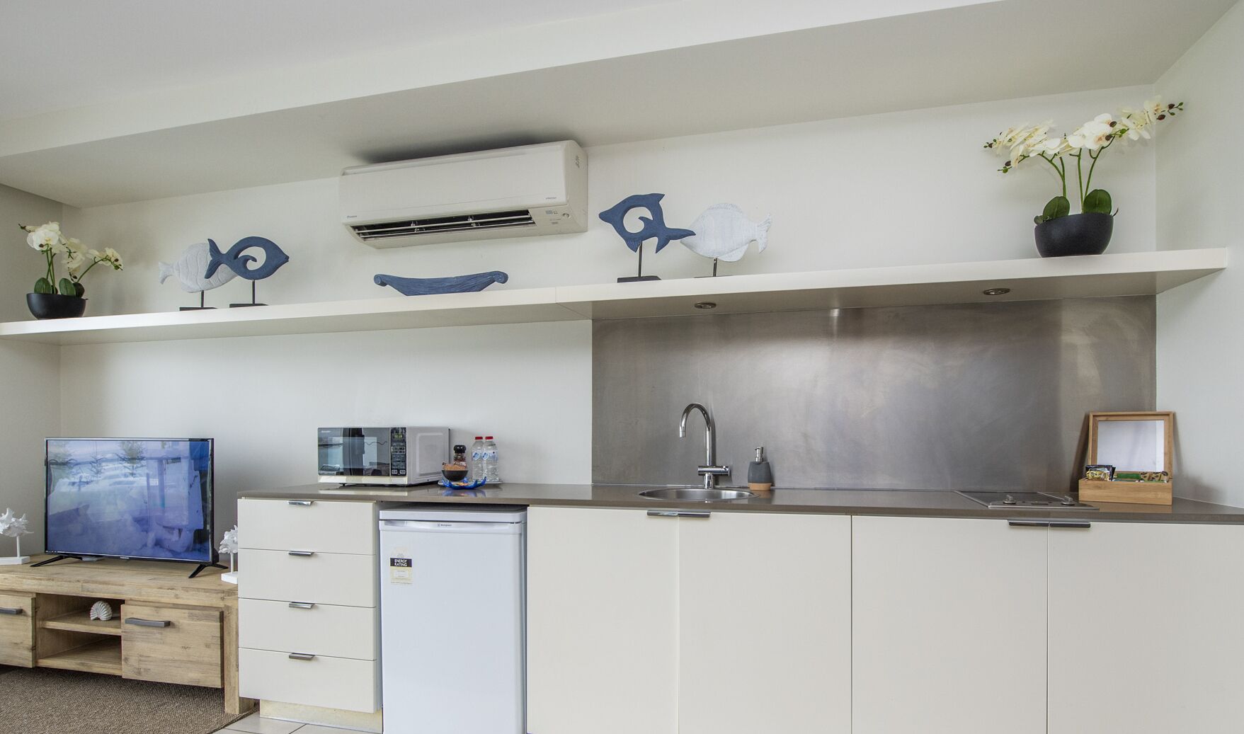Cozinha moderna com armários brancos, micro-ondas embutido, pia e esculturas decorativas de peixes.