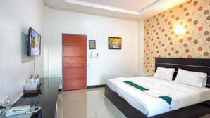 A hotel room with a bed, a television, a door, and a wall with floral wallpaper. - Phuthan Hotel (Tha Chang)