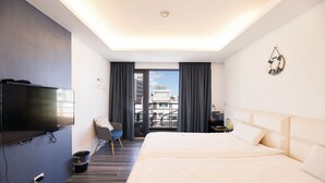 A modern hotel room with a large bed, a flat-screen TV mounted on the wall, a chair, and a view of the city through the balcony doors. - Cypress Inn (Taitung)